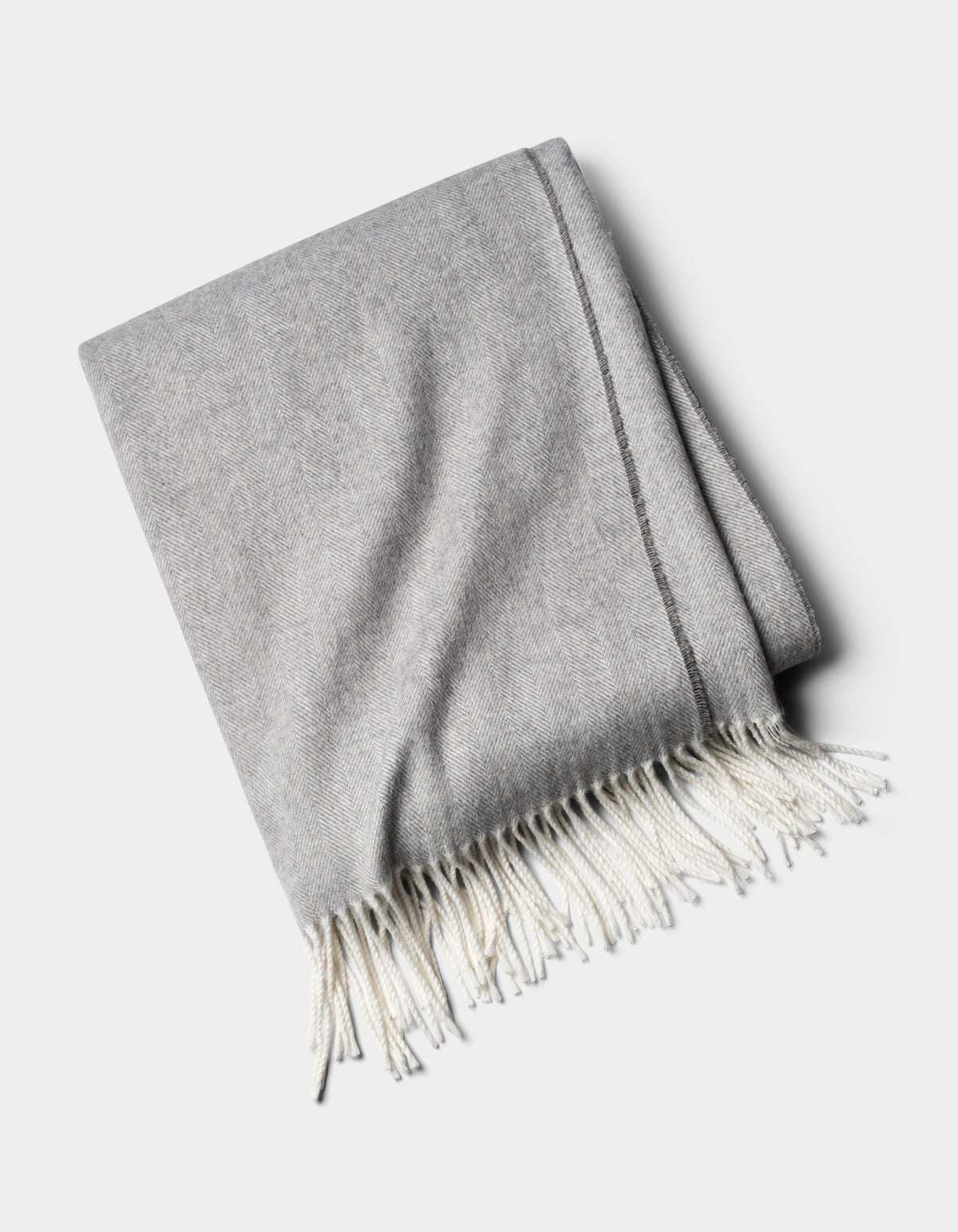 The Cozy Earth Bamboo Herringbone Tassel Throw is a folded light gray blanket with white fringed tassels on one edge, shown against a plain white background.|Color:Cloud