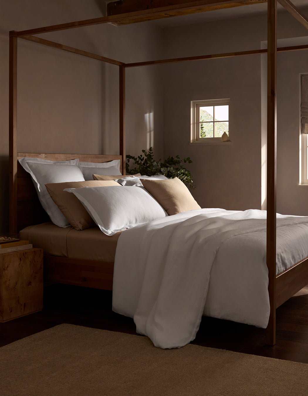 A cozy bedroom features a wooden four-poster bed with a Cozy Earth Linen Duvet Cover, soft light streaming through small windows, and a plant on the nightstand, creating a calm and inviting atmosphere.|Color:White