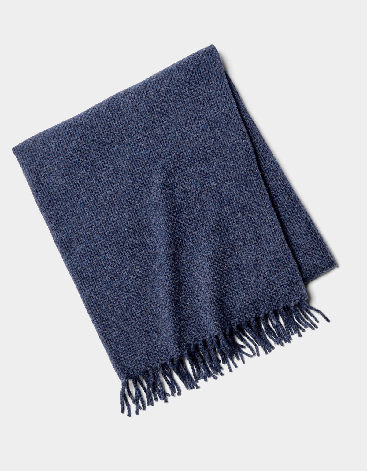 The Cozy Earth Lucia Throw, a folded dark blue woven blanket with fringe tassels on one edge, is displayed against a light gray background.|Color:Indigo