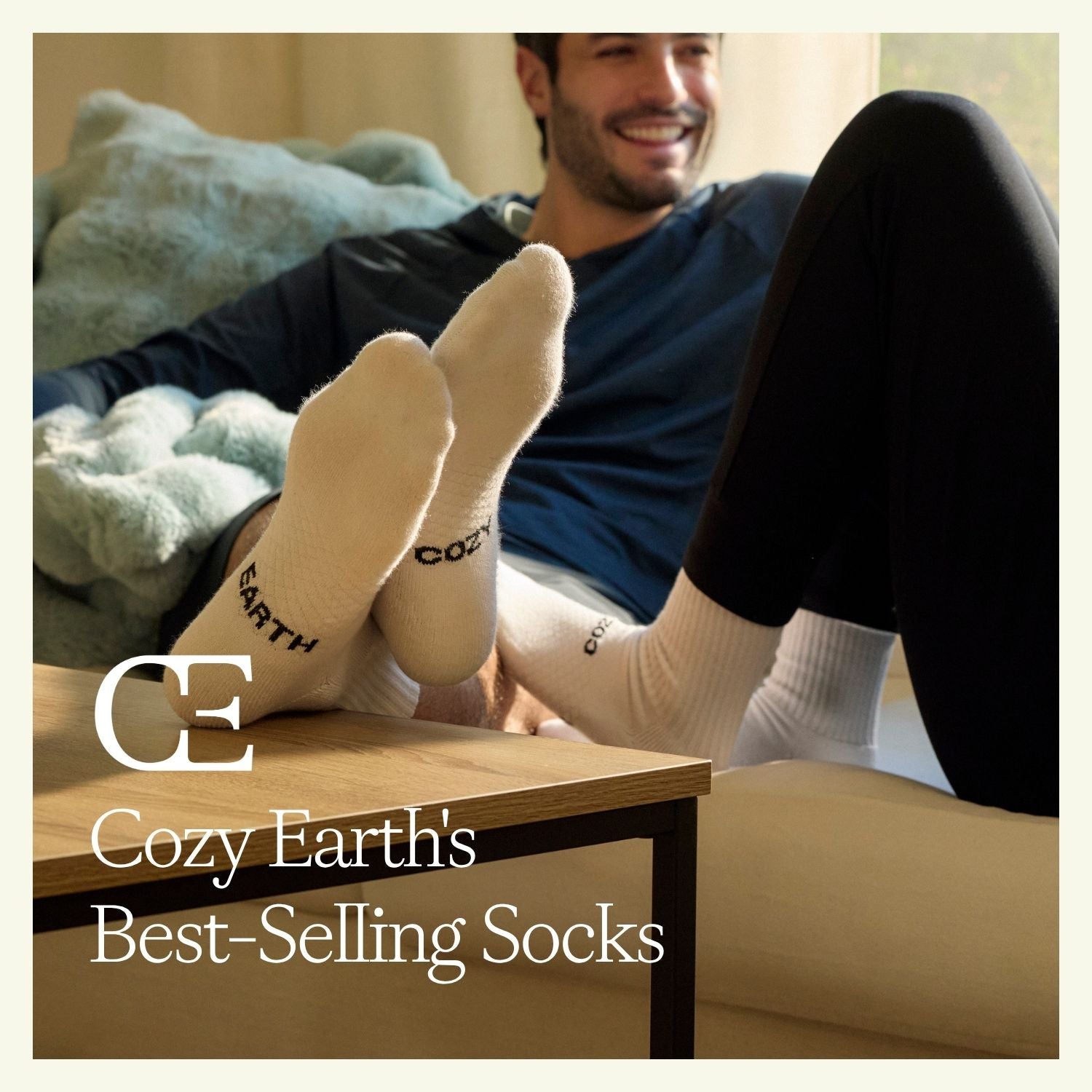 A close up of a man's feet resting on a table. He wears white Cozy Earth Essential Socks