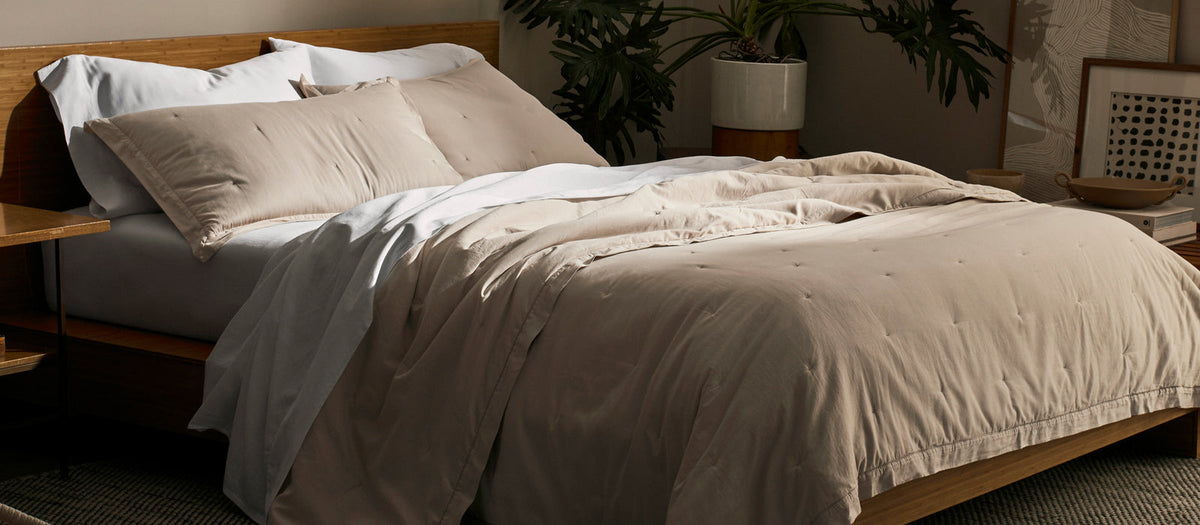 A bed made with taupe Cozy Earth Soft Wash Quilt and sheets in a warmly lit, neutral bedroom