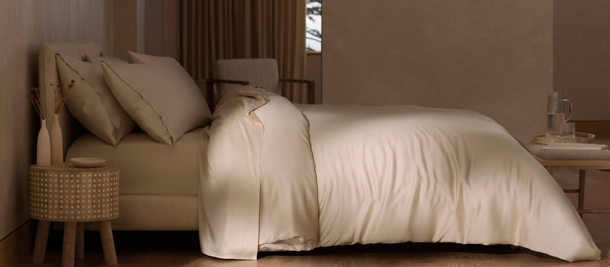 A bed featuring Cozy Earth sheets and duvet cover in Driftwood with a bedside table and soft, neutral lighting