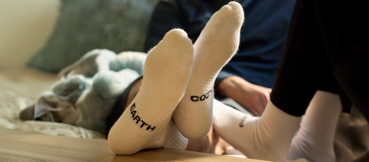 A man's feet crossed on a table wearing white Cozy Earth socks