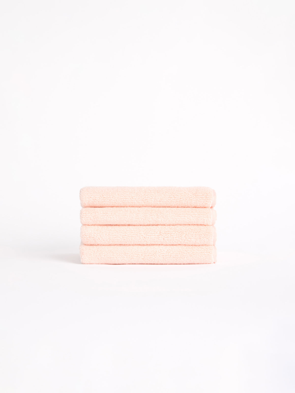 Four neatly folded Luxe Washcloths in light pink from Cozy Earth sit against a plain white backdrop. 