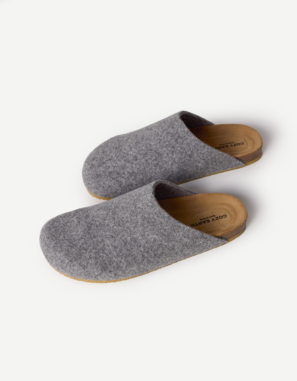 The Lakehouse Clog by Cozy Earth features a minimalist design with grey woolen uppers and natural brown soles. It has a closed toe, open back, and is ideal for indoor wear. A logo is visible on the insole, all showcased on a white background. 