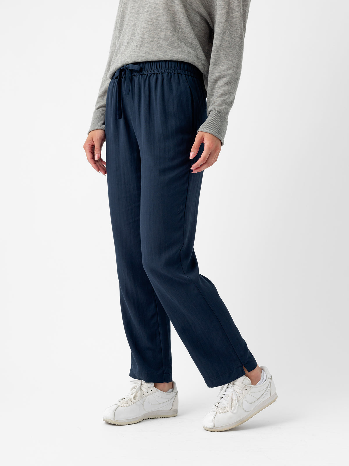 A person wearing a gray long-sleeve top and the Women's Sunset Cropped Pant from Cozy Earth in navy blue stands against a white background. They are also wearing white sneakers. The person's face is not visible. |Color:Eclipse