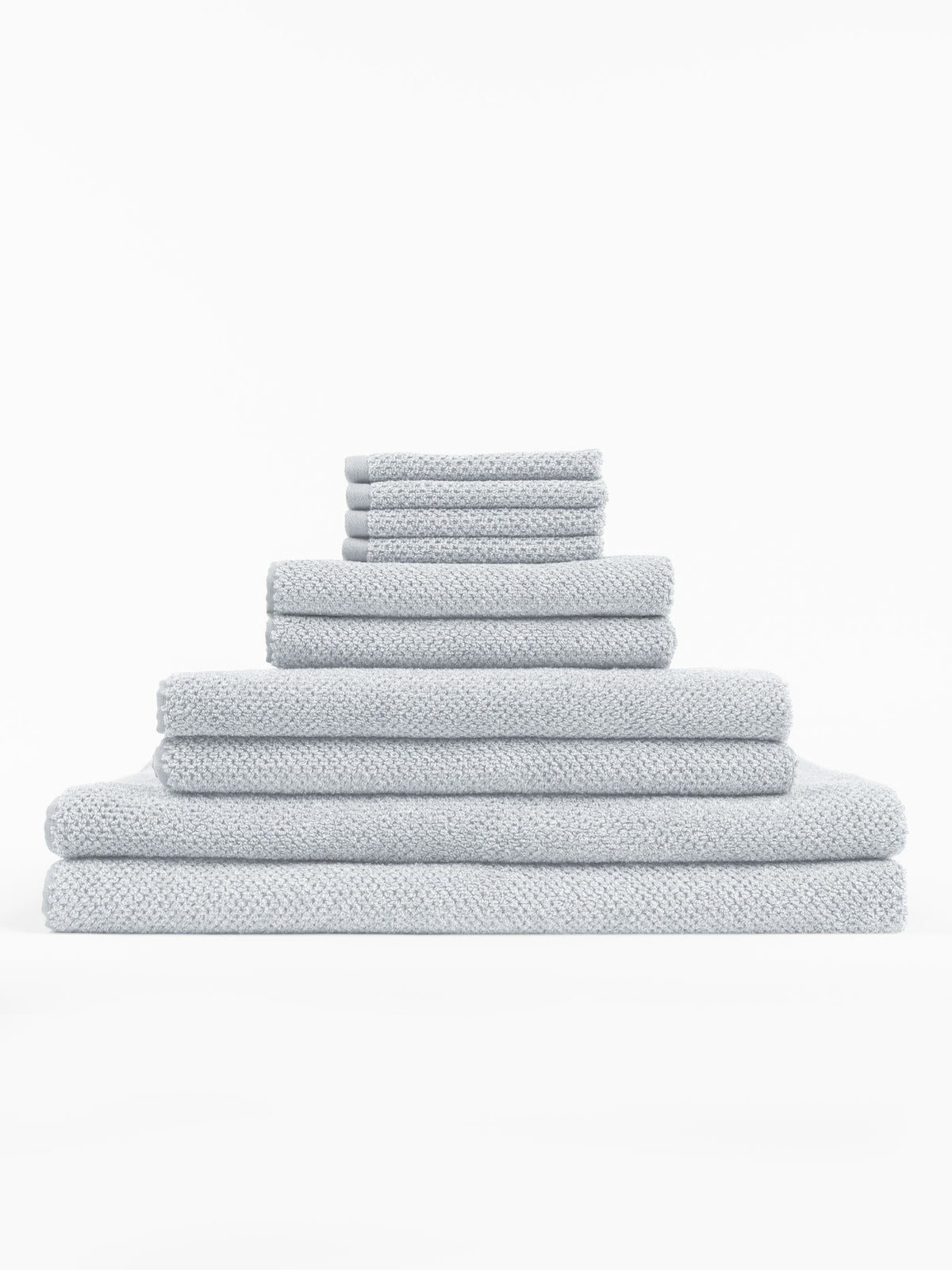 The Cozy Earth Complete Nantucket Bath Bundle features light gray textured towels in assorted sizes, neatly stacked in a pyramid formation against a plain white background.