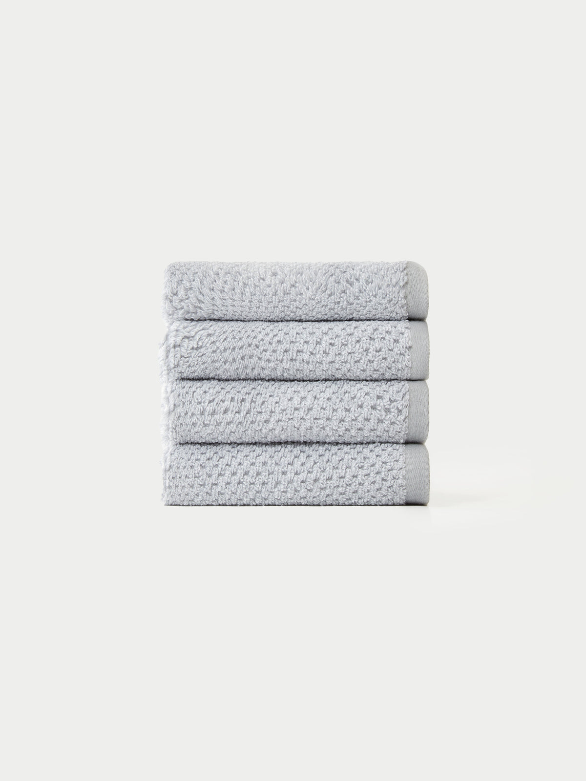 A neatly stacked pile of four light gray, textured towels from the Cozy Earth Nantucket Bath Towel Set on a plain white background.