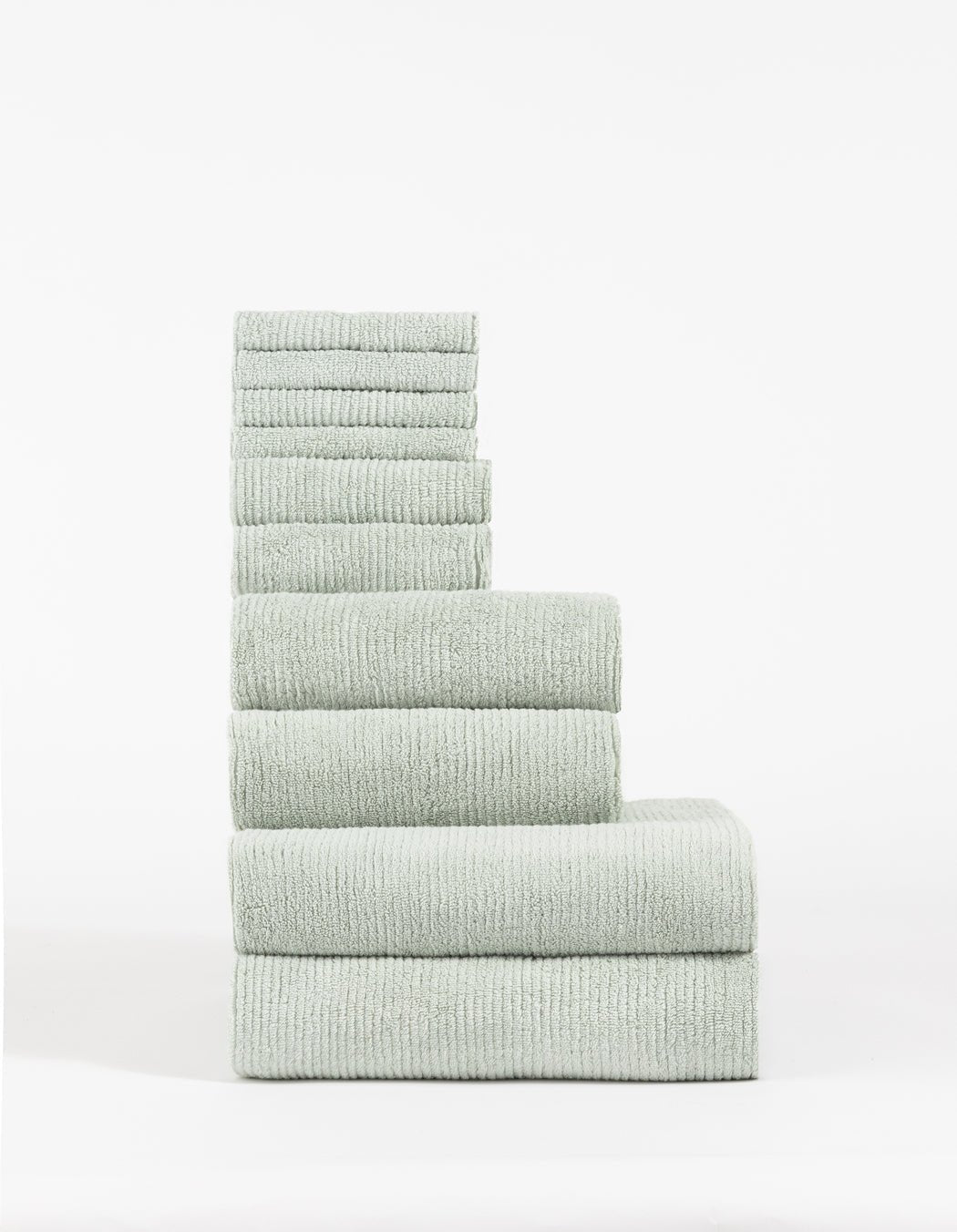 The Cozy Earth Complete Ribbed Terry Bath Bundle features a stack of light gray, ribbed towels in descending size order, arranged neatly against a plain white background.