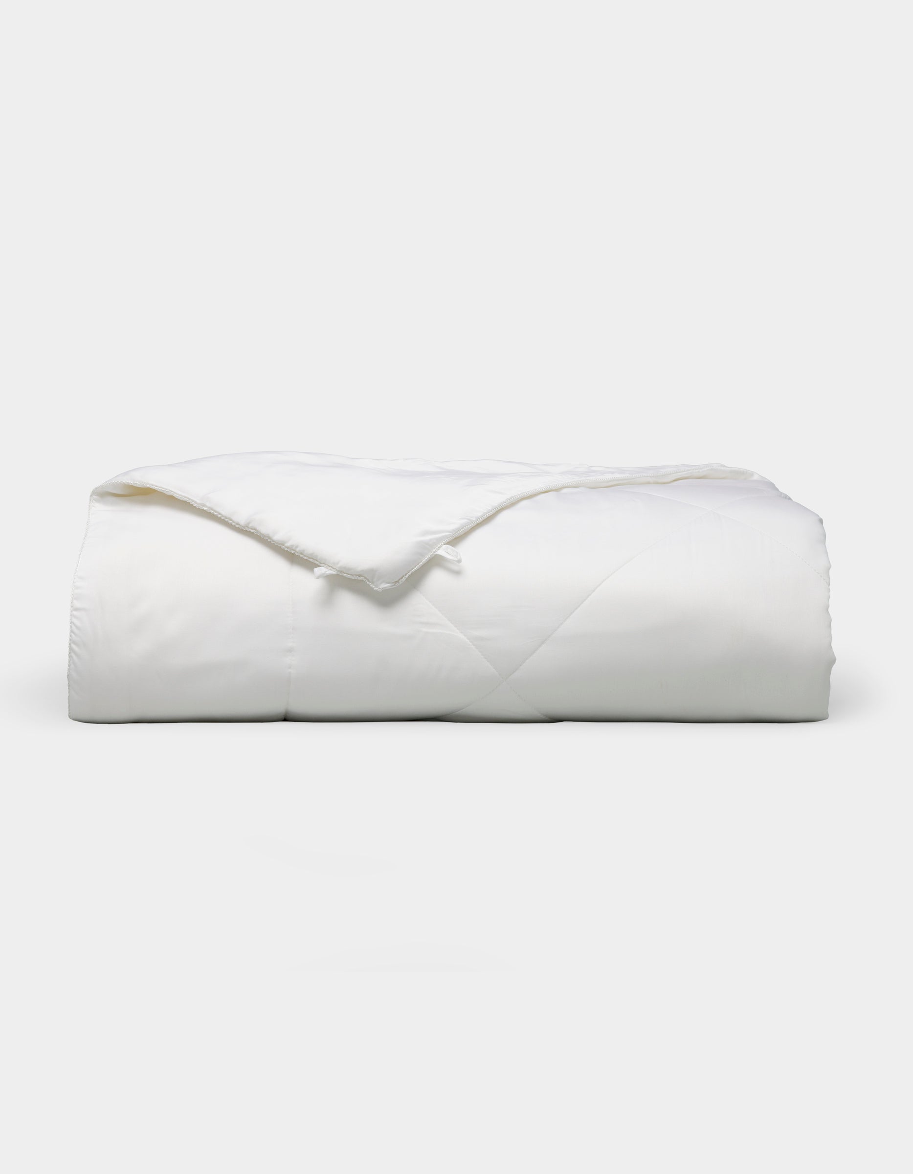 The Bamboo Viscose All Season Comforter by Cozy Earth, featuring a neatly folded white design with a subtle sheen, is displayed against a plain light background.|Filling:Standard 