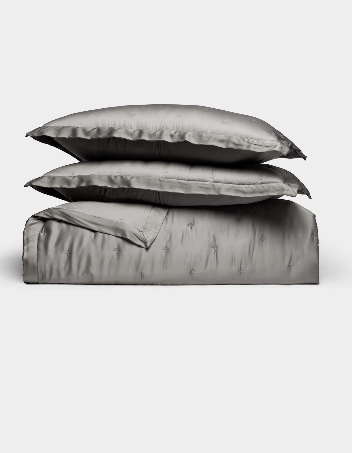 The Bamboo Quilt Bundle by Cozy Earth features lustrous silver-gray bed linens, including two stacked pillows, a folded sheet, and a duvet cover, all arranged against a plain white background.