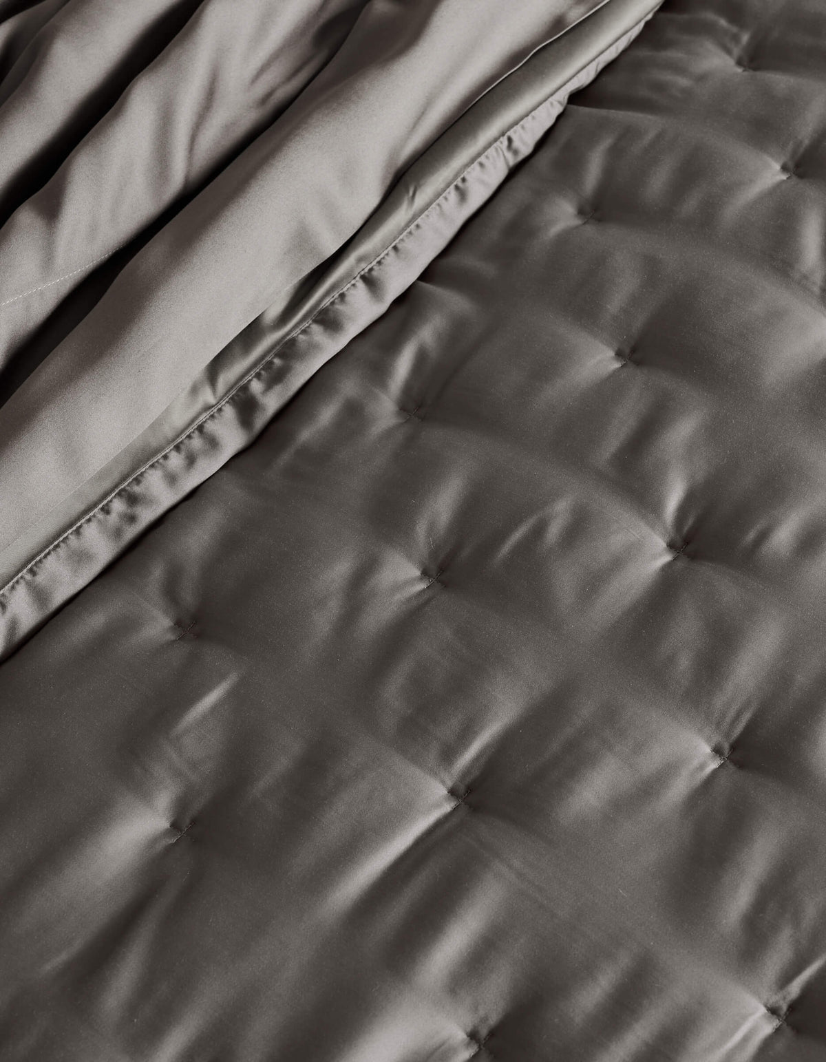 A close-up of the Cozy Earth Bamboo Quilt, neatly folded, showcasing its quilted dark gray design with smooth, satin-like texture and square stitching.