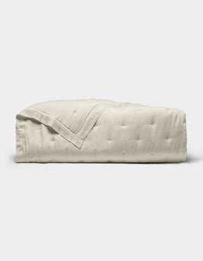 The Cozy Earth Bamboo Quilt, featuring a subtle quilted pattern and light beige color, is neatly folded and displayed against a plain white background.|Color:Oat