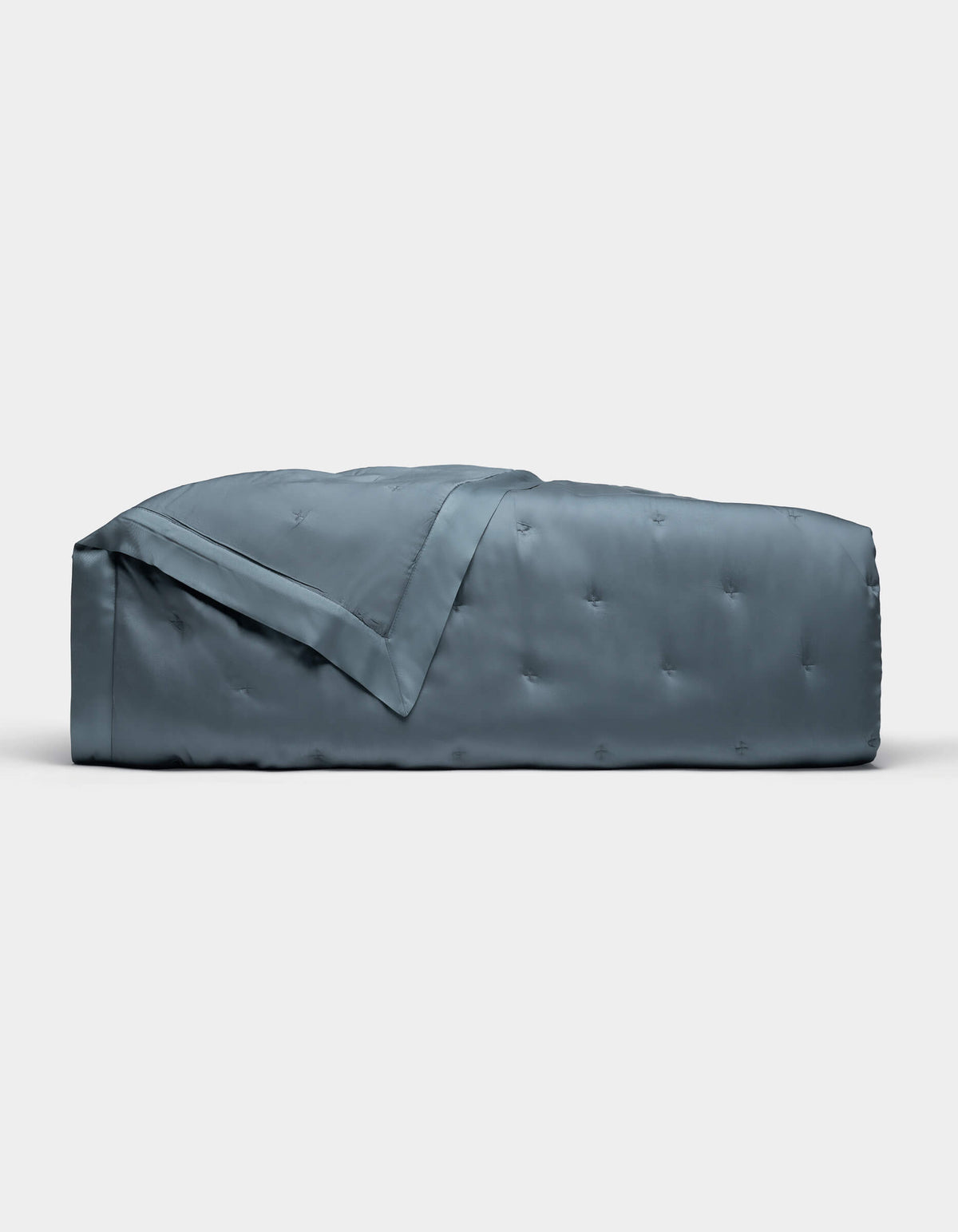 The Cozy Earth Bamboo Quilt, shown folded against a plain white background, features a blue-gray color with a subtle quilted pattern and smooth, shiny finish.