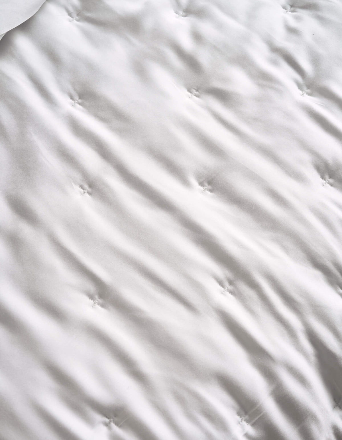 A close-up of the Cozy Earth Bamboo Quilt’s white, tufted surface features gentle waves and sewn dimples, hinting at its soft, quilted texture.