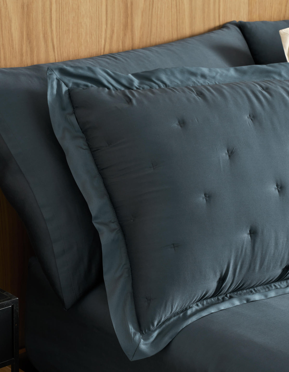 A close-up of a neatly made bed features Cozy Earth Bamboo Quilted Shams and matching sheets in dark blue, set against a light wood headboard.