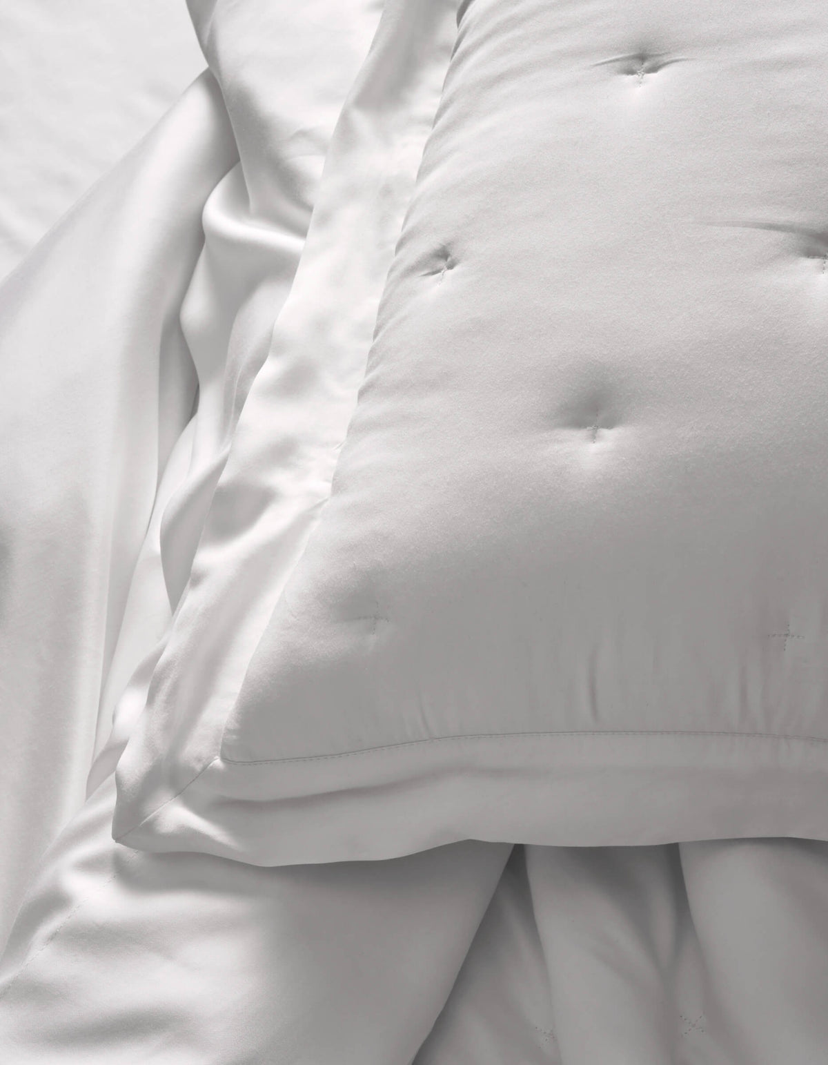 A close-up of Cozy Earth Bamboo Quilted Shams resting on smooth white sheets creates a soft, clean look. The bedding appears fluffy and inviting.