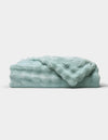 The Bubble Cuddle Blanket by Cozy Earth, in a soft light blue, is shown folded neatly on a white background.|Color:Tide