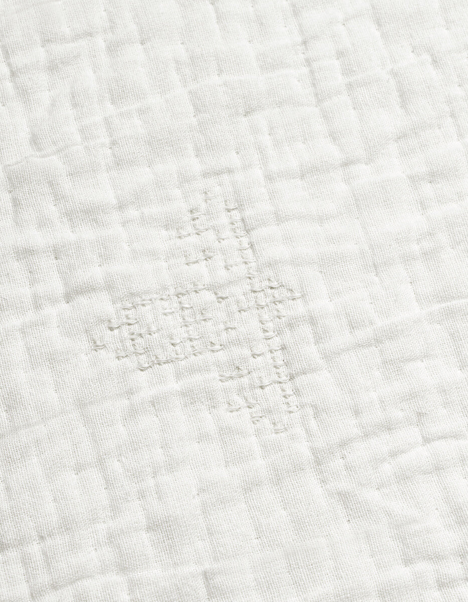 A close-up of the Cozy Earth Little Bee Matelasse Baby Blanket shows its grey fabric with a grid-like, hand-stitched repair in matching thread, highlighting the textured and slightly uneven surface.