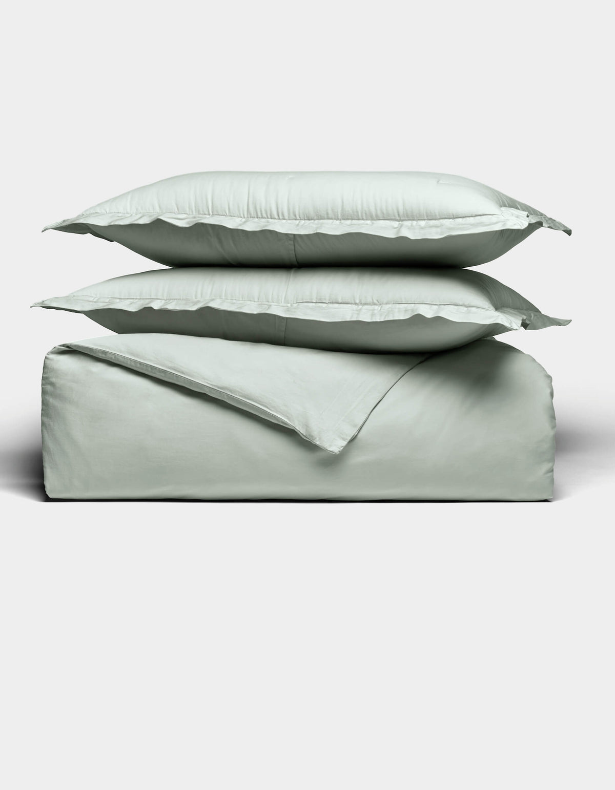 Two light gray pillows are stacked atop a matching folded Soft-Wash Cotton Duvet Set by Cozy Earth, all set against a plain white background. The bedding appears soft and smooth, highlighting its cozy and minimal aesthetic.|Color:Laurel