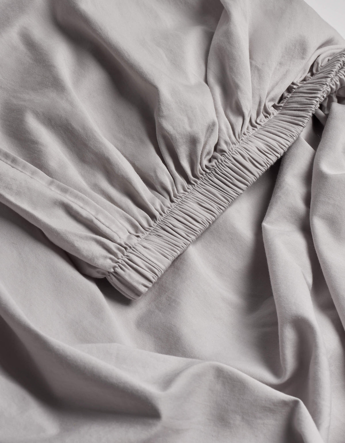 A close-up of the Cozy Earth Soft-Wash Cotton Fitted Sheet highlights its light gray color, gathered elastic edge, and ultra-soft fabric texture.