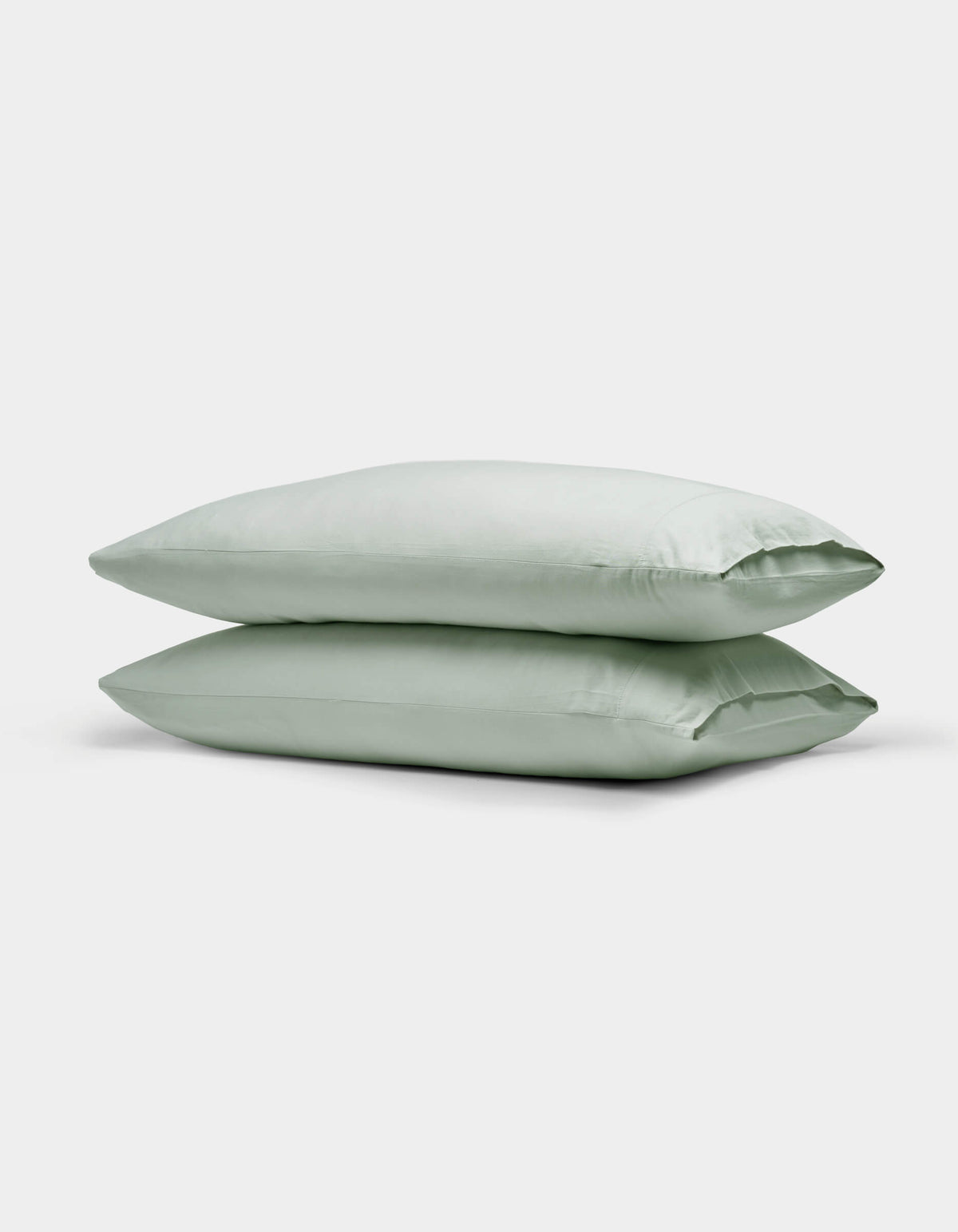 Two Cozy Earth Soft-Wash Cotton Pillowcases in light green are neatly stacked against a plain white background.|Color:Laurel