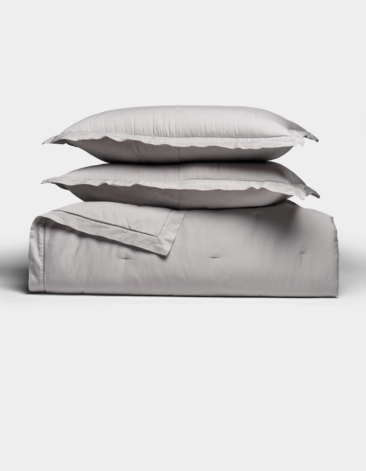 Two light gray pillows rest atop a folded Soft-Wash Cotton Quilt Set by Cozy Earth, arranged neatly against a plain white background. The bedding looks exceptionally soft and inviting.