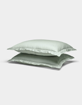 Two Soft-Wash Cotton Shams by Cozy Earth in light green are stacked atop each other against a plain white background.|Color:Laurel