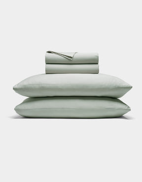 The Cozy Earth Soft-Wash Cotton Sheet Set includes a neatly folded light gray fitted and flat sheet with two stacked pillows, displayed against a plain white background.|Color:Laurel