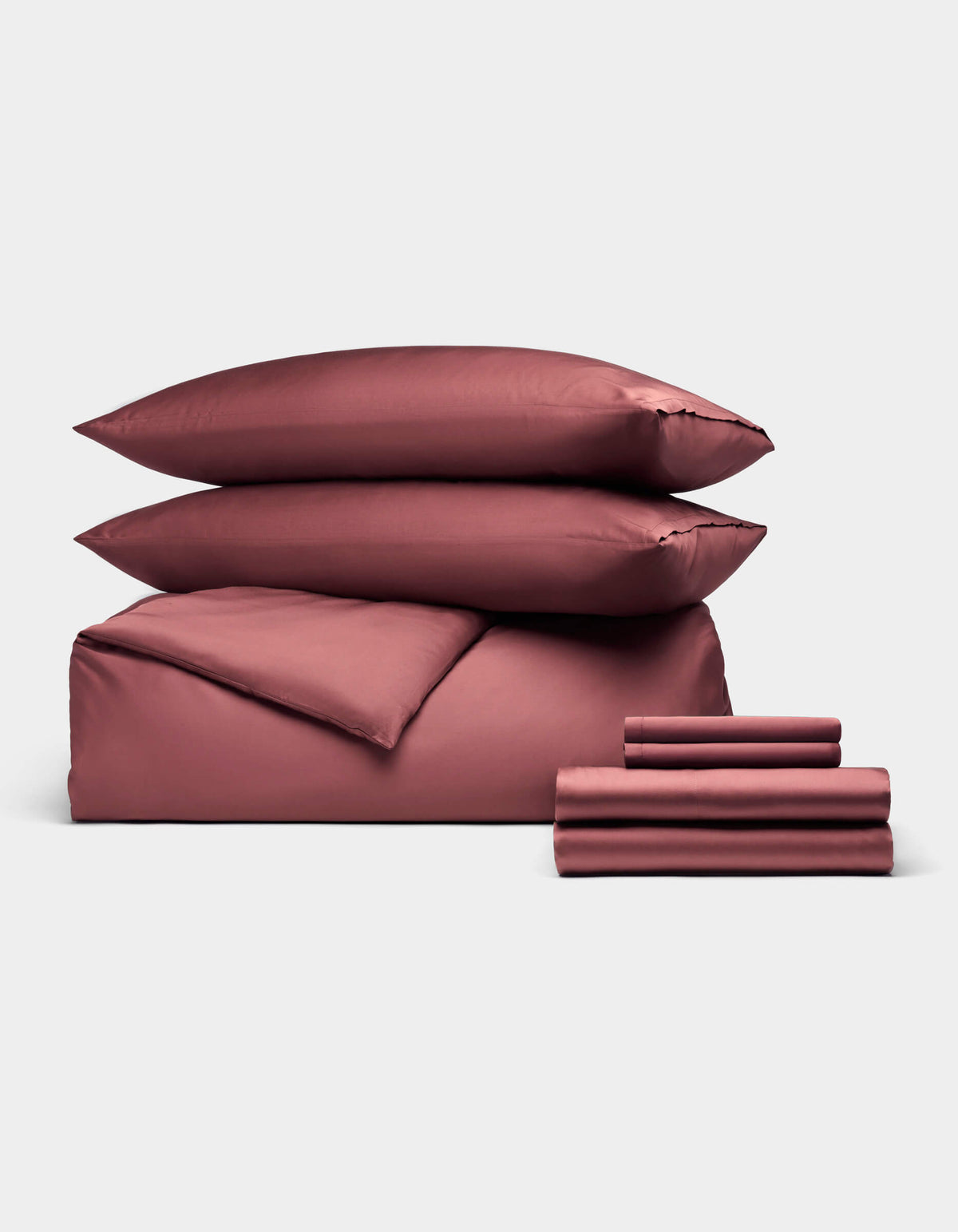 The Cozy Earth Bamboo Bedding Ultimate Bundle features two pillows, a duvet cover, and folded sheets in mauve, all elegantly displayed against a plain light gray background.