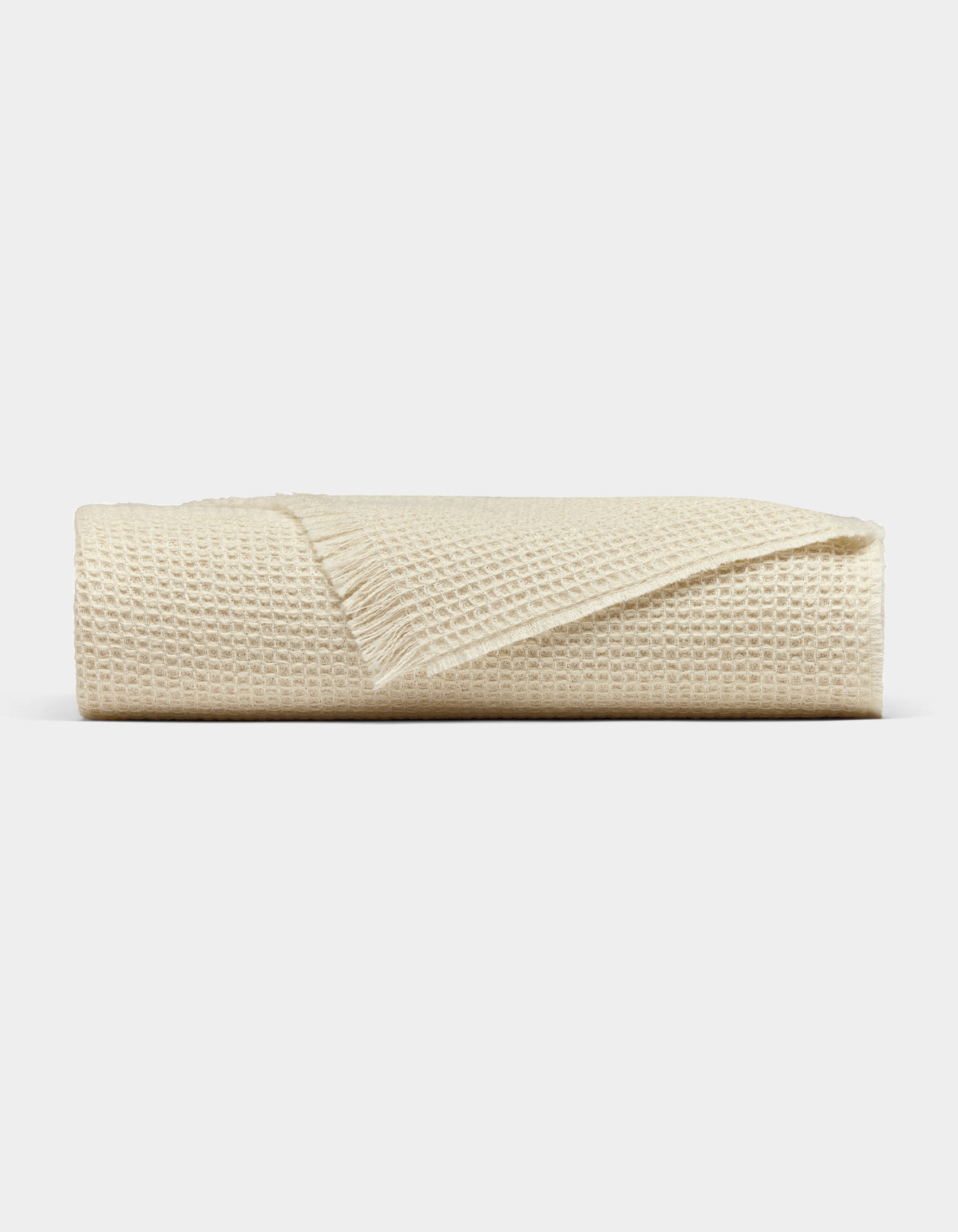 The Cozy Earth Alpaca Waffle Throw, in beige with a fringed edge, is neatly folded and displayed against a plain light gray background.