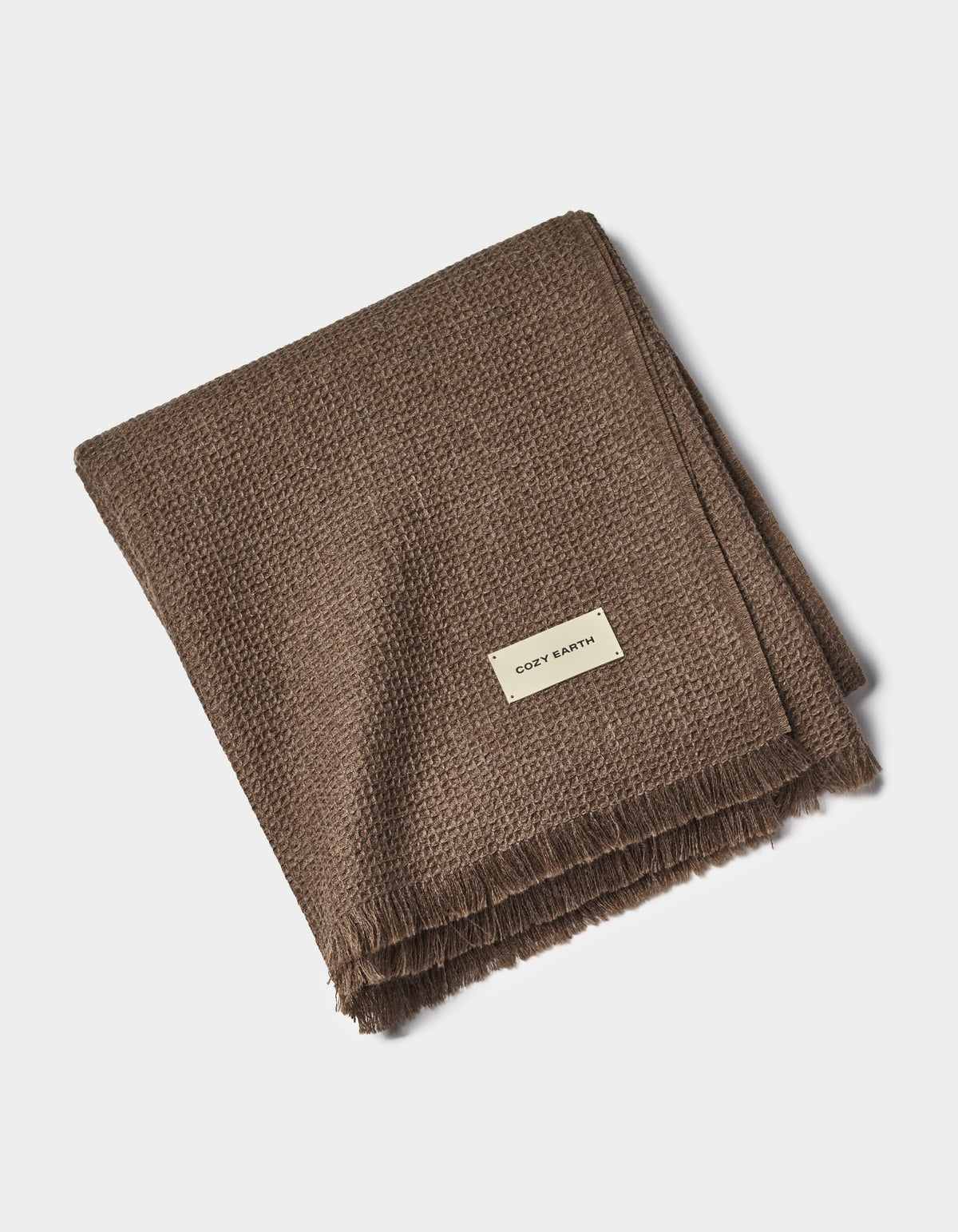A folded brown Alpaca Waffle Throw by Cozy Earth with fringed edges and a small rectangular "Cozy Earth" label, displayed on a plain white background.