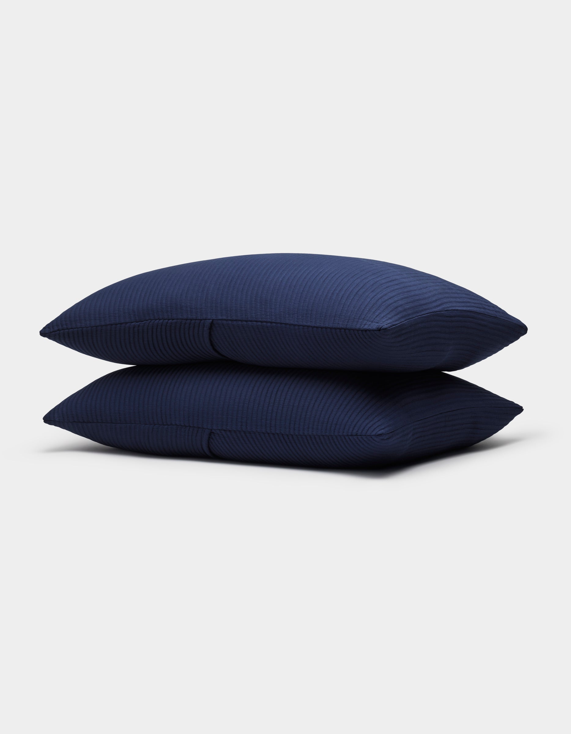 Two Bamboo Coverlet Shams by Cozy Earth, in dark blue with a subtle striped texture, are neatly stacked against a plain light gray background.|Color:Navy