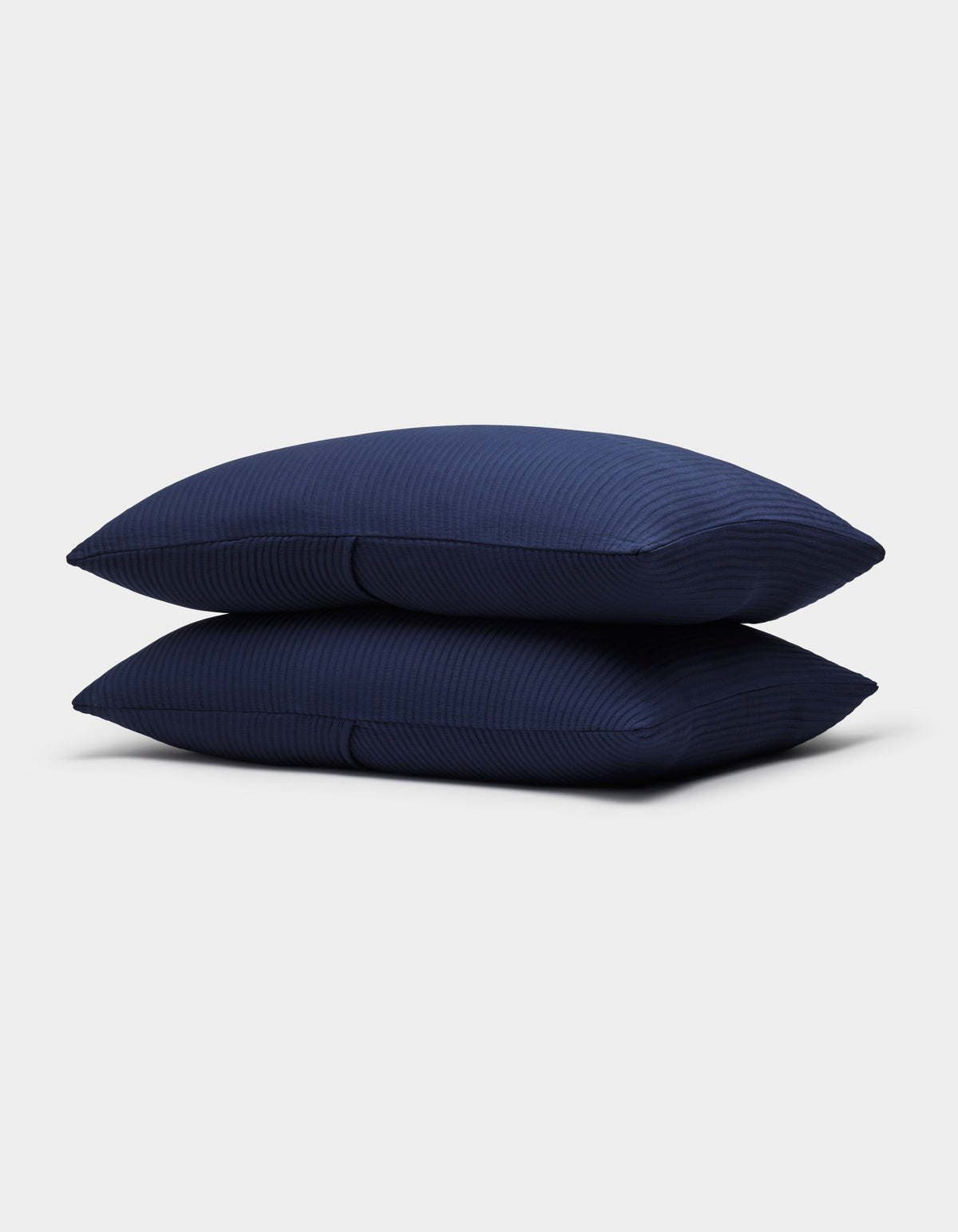 Two Bamboo Coverlet Shams by Cozy Earth, in dark blue with a subtle striped texture, are neatly stacked against a plain light gray background.