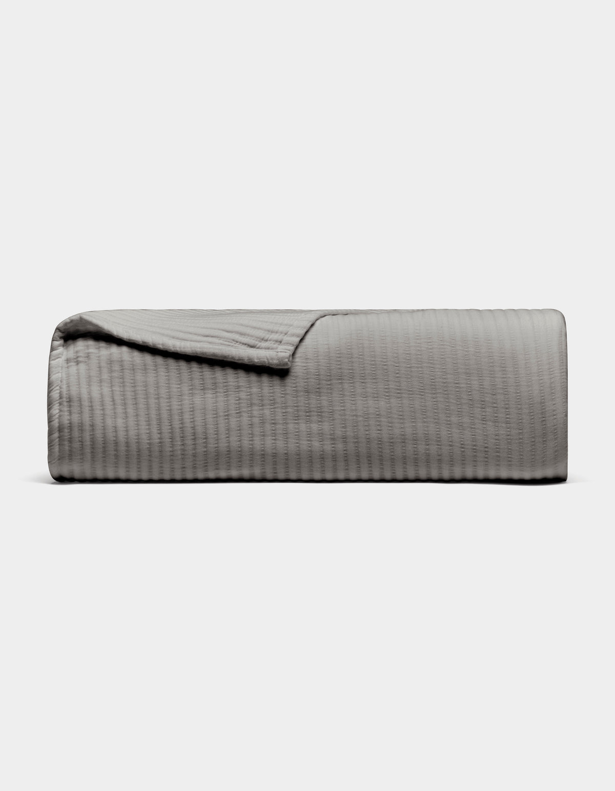 The Cozy Earth Bamboo Coverlet, shown neatly folded in light gray with a subtle textured pattern, is displayed on a plain white background. One corner is turned down to reveal the inner side of the coverlet.|Color:Charcoal