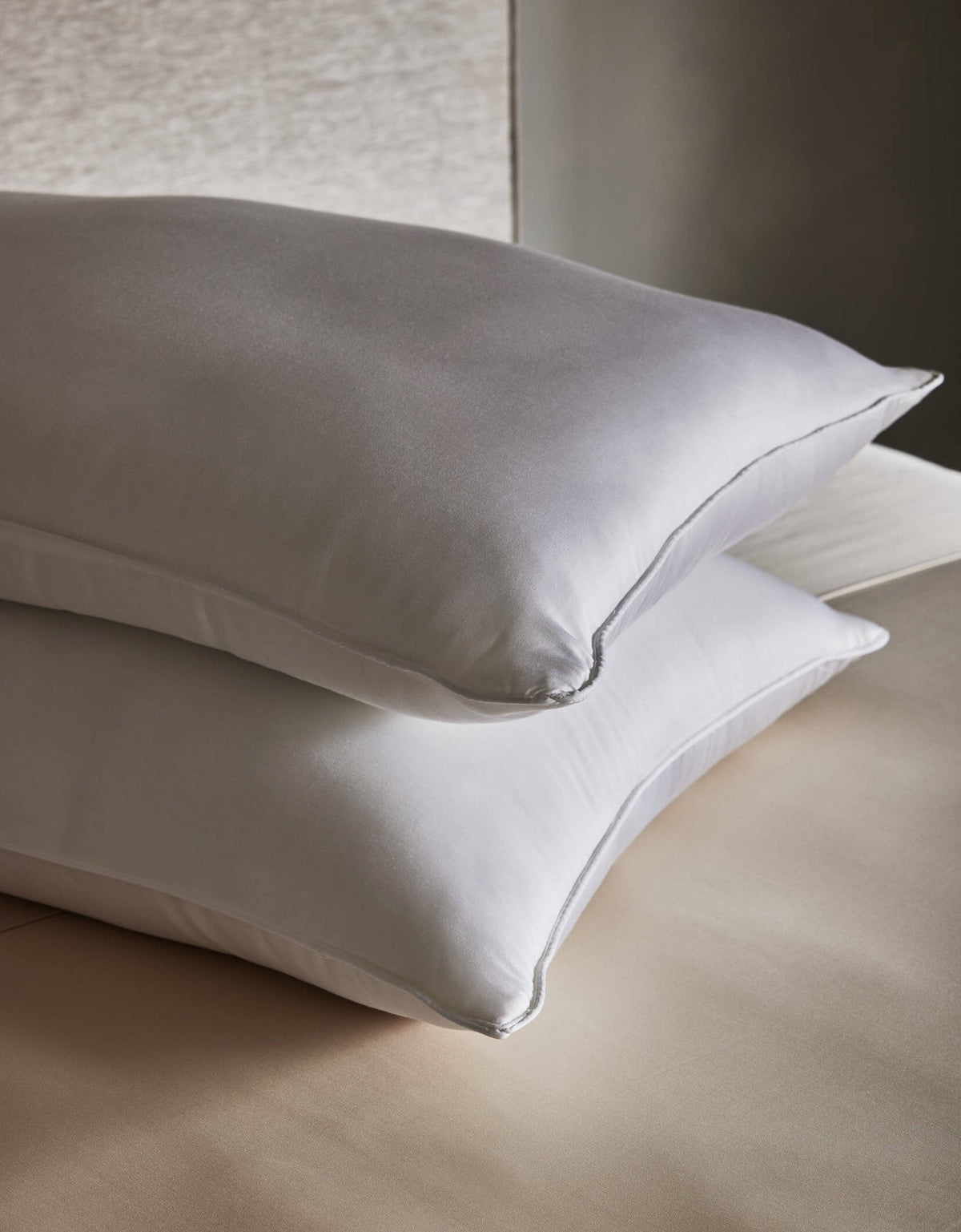 Two Cozy Earth Down Alternative Insert Bundle pillows are stacked on a light beige bed, set against a soft, neutral background for a calm and serene atmosphere.