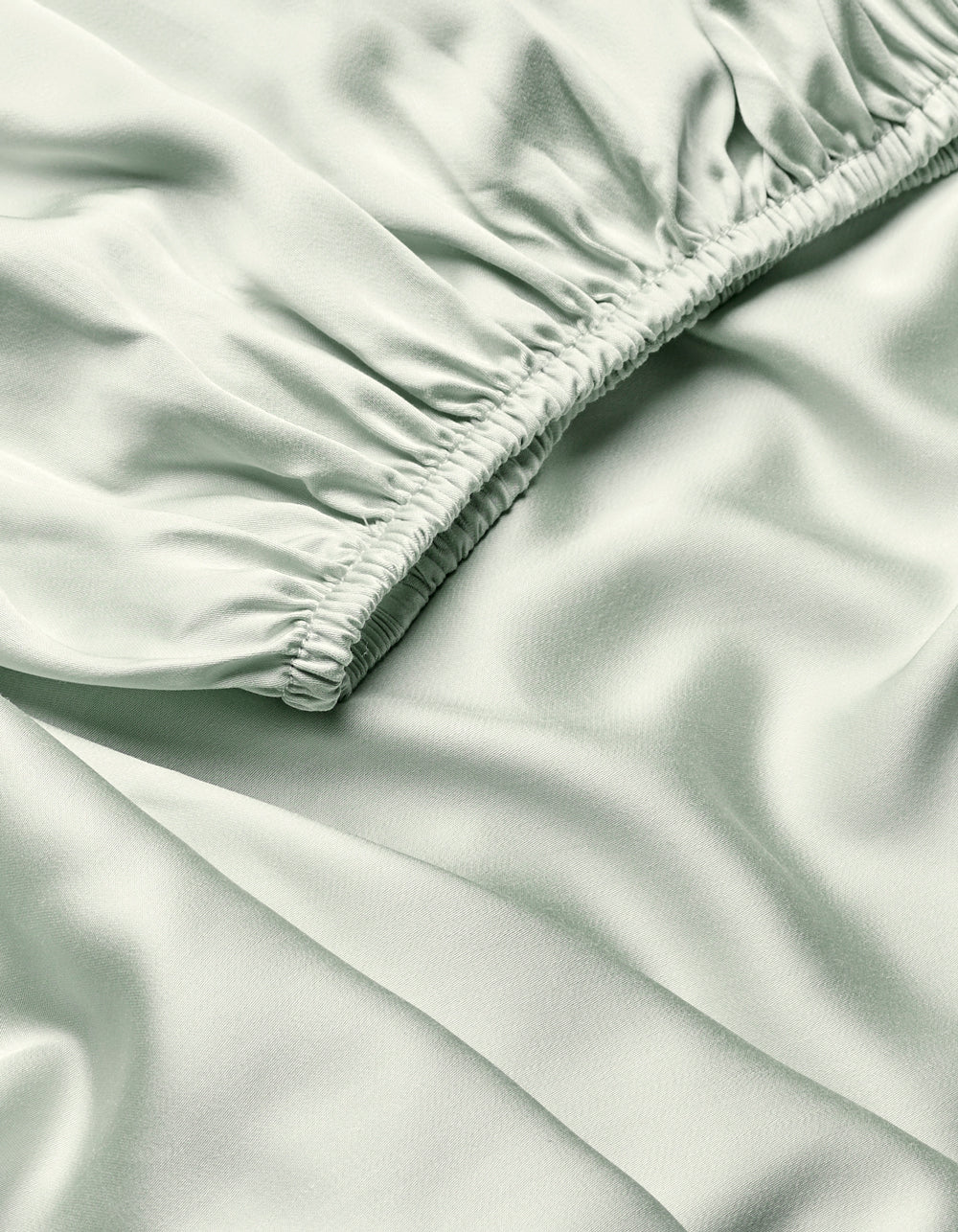 Close-up of Cozy Earth’s Bamboo Fitted Sheet in light green, showing silky fabric with a diagonal ruched seam that creates soft folds and a smooth, shiny texture.