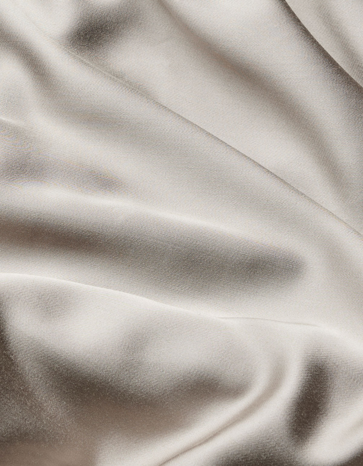 The Bamboo Flat Sheet by Cozy Earth features smooth, cream-colored satin fabric with gentle, flowing folds and a soft sheen that beautifully reflects light.