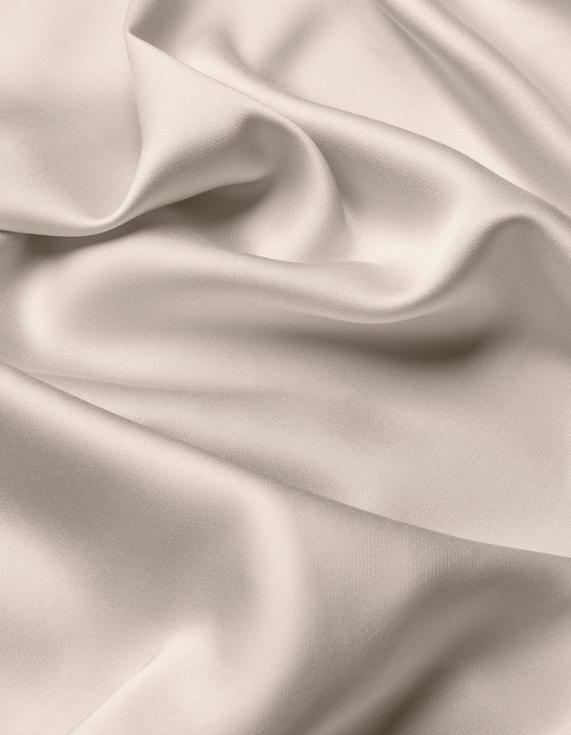 The Cozy Earth Bamboo Sheet Set features smooth, light-colored satin fabric with gentle folds and soft shadows for a flowing, elegant texture.