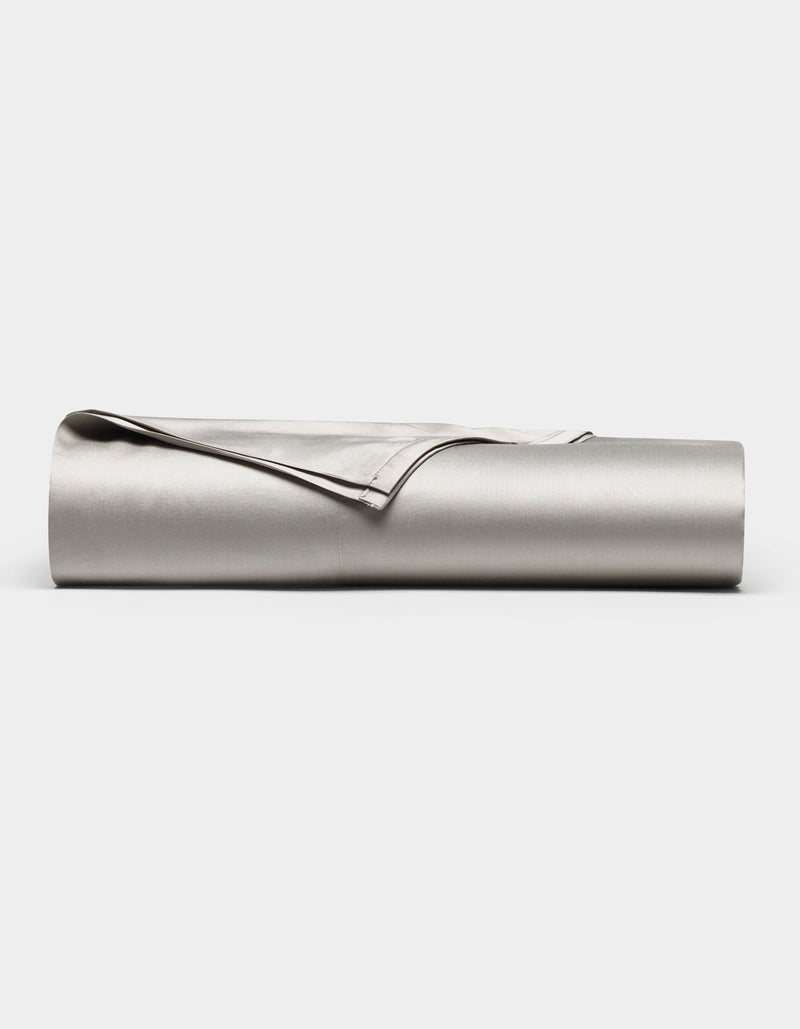 The Cozy Earth Bamboo Flat Sheet, shown in light gray with one corner folded over, is neatly rolled up and displayed against a plain white background.