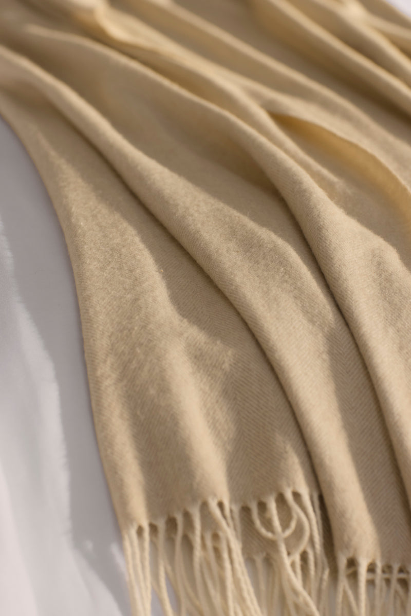 The Cozy Earth Bamboo Herringbone Tassel Throw, featuring a subtle herringbone texture and tasseled edges, is draped over a white surface in gentle folds.