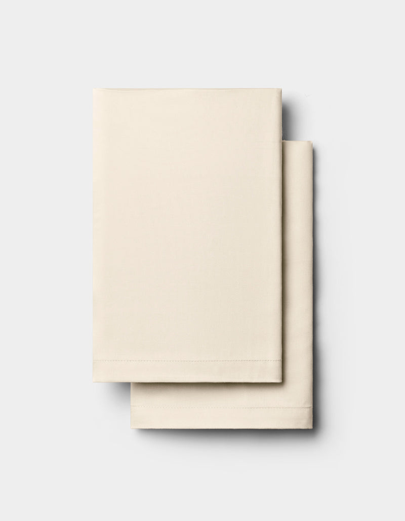 Two neatly folded, cream-colored rectangular Bamboo Pillowcases by Cozy Earth are stacked on top of each other against a plain, light gray background.