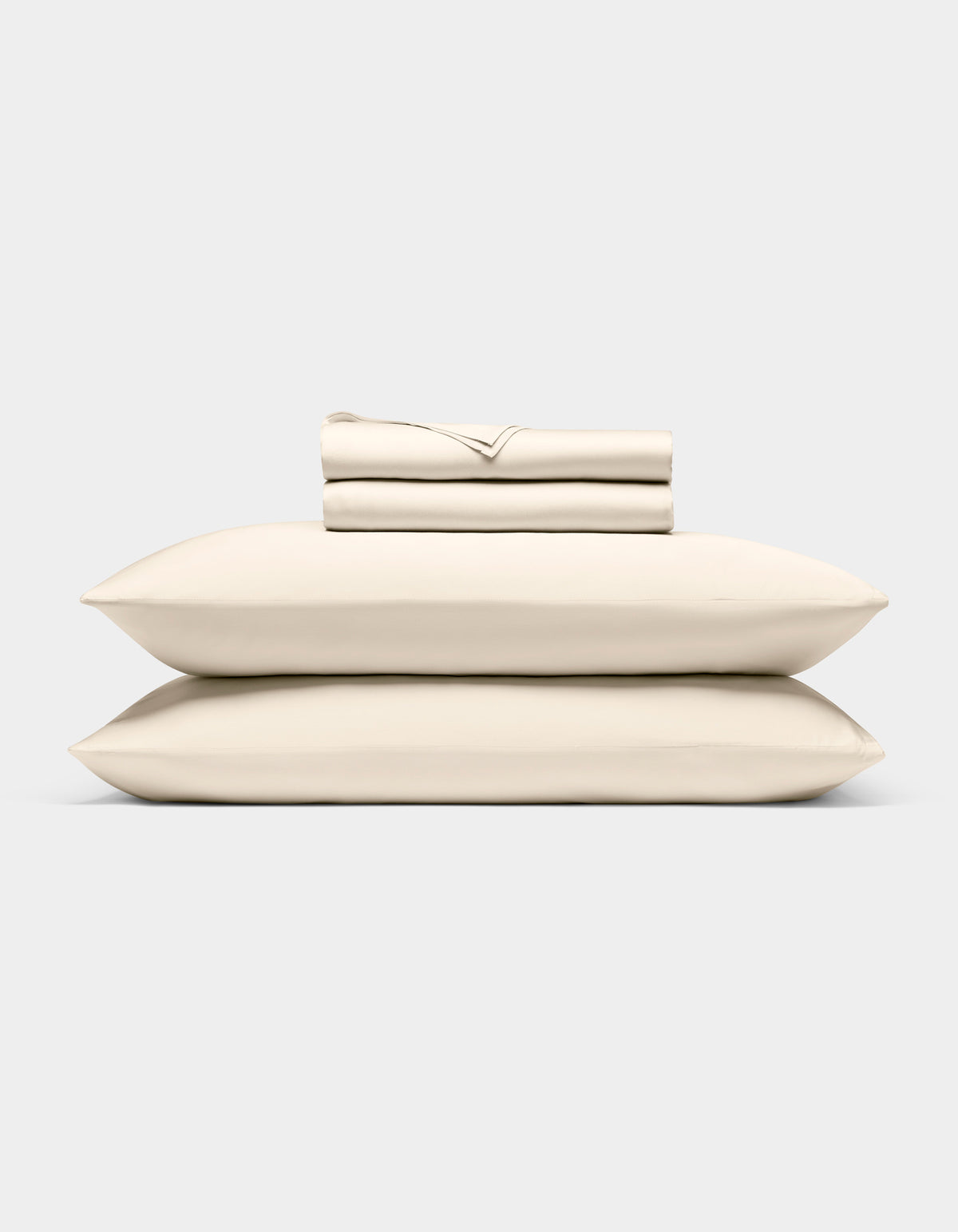 The Cozy Earth Bamboo Sheet Set, neatly folded in cream, rests atop two matching pillows against a light gray background.|Color:Creme