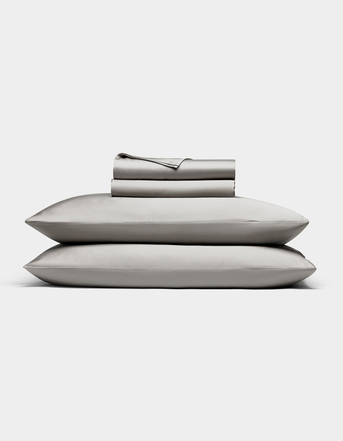 The Bamboo Sheet Set by Cozy Earth in light gray is neatly folded, with two pillows stacked and both flat and fitted sheets rolled on top, all displayed against a white background.|Color:Light Grey