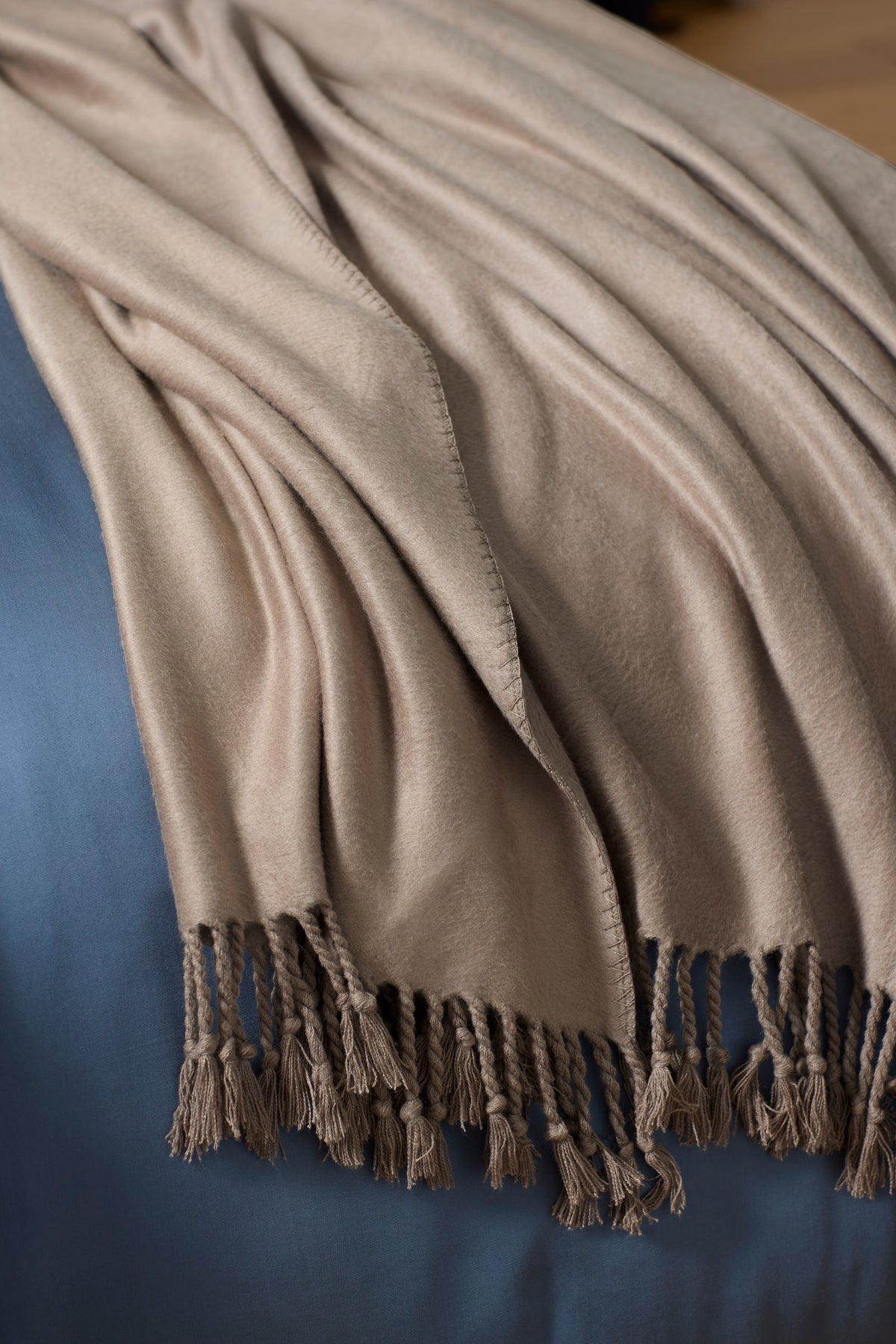 The Cozy Earth Bamboo Tassel Throw, featuring tasseled edges, is draped over a blue surface, forming soft folds and a cozy look.