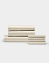 The Cozy Earth Bamboo Bedding Core Bundle, featuring cream-colored bed sheets and pillowcases, is neatly folded in two stacks against a plain white background.|Color:Creme