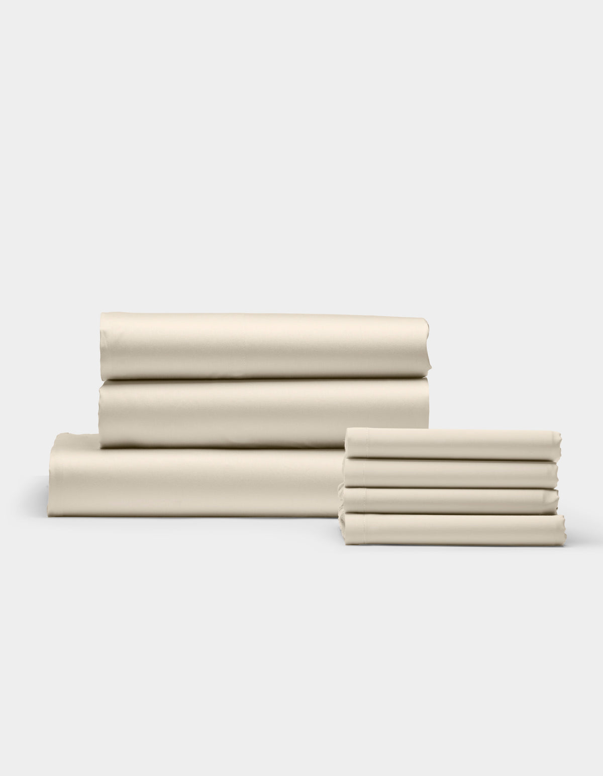 The Cozy Earth Bamboo Bedding Core Bundle, featuring cream-colored bed sheets and pillowcases, is neatly folded in two stacks against a plain white background.|Color:Creme