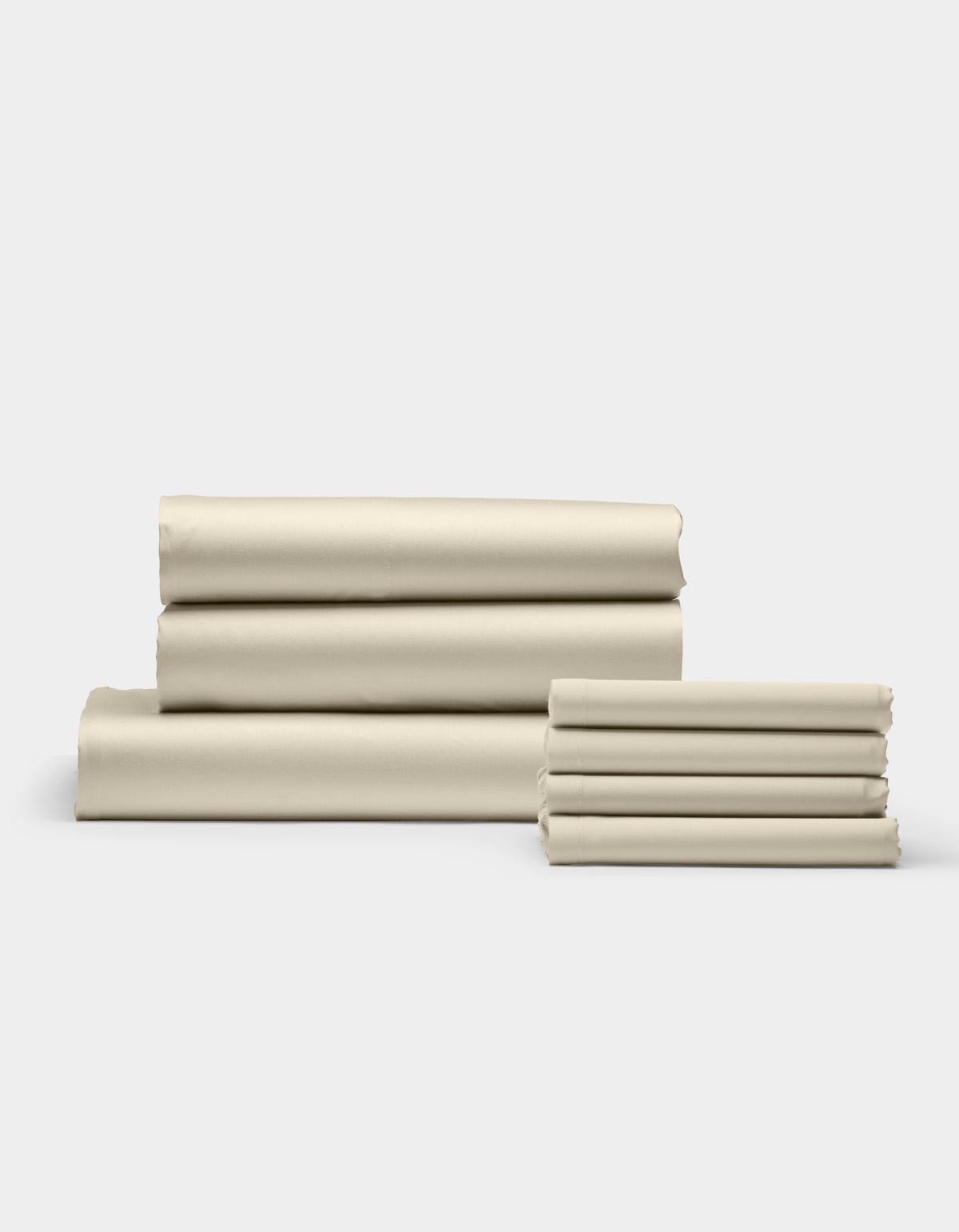 Cozy Earth’s Bamboo Bedding Core Bundle is shown in stacks of neatly folded beige sheets, arranged on a white surface with a light gray background. The smooth sheets are organized into one large and one small pile.|Color:Oat