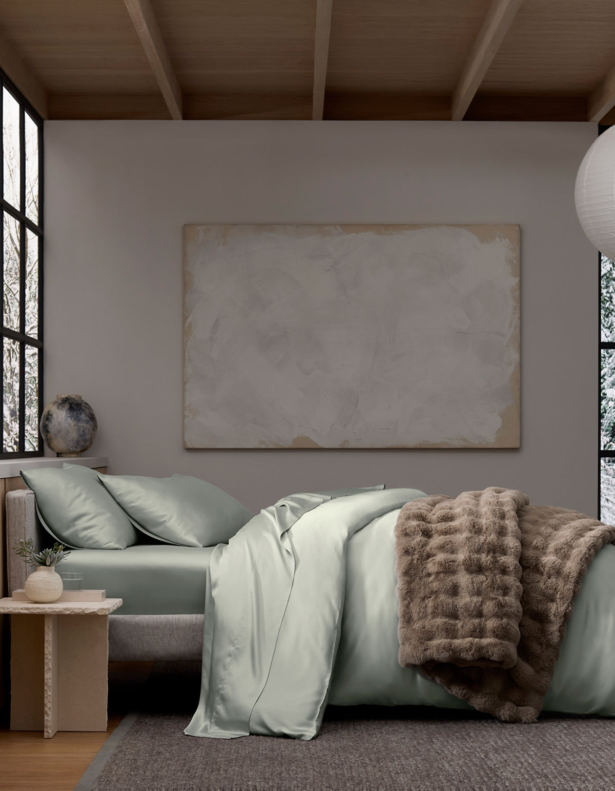 A modern bedroom with a Cozy Earth Bamboo Duvet Cover in light gray, a plush fur throw, large abstract art above the bed, a side table with a vase, and big windows filling the space with natural light.