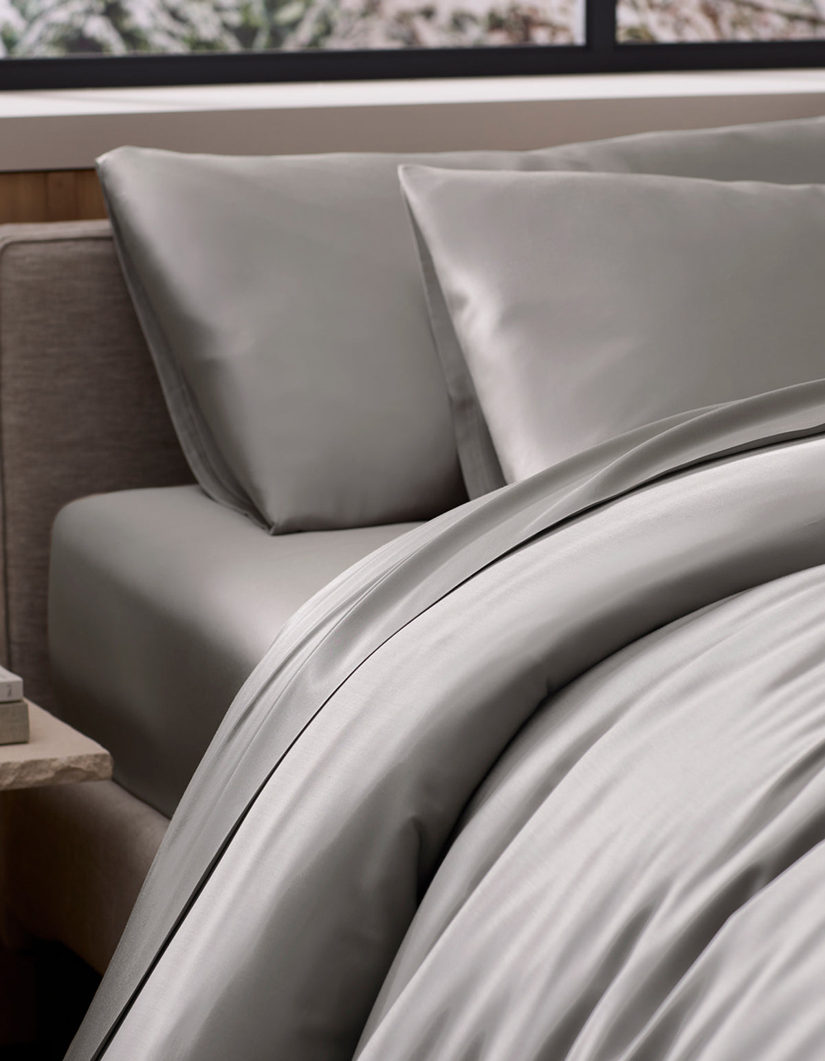 A neatly made bed features the Cozy Earth Bamboo Duvet Cover in light gray with dark trim, paired with matching pillowcases. The bed is near a window with an outdoor view and has a nightstand beside it.